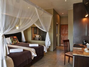 A hotel room with a bed, a small table, a chair, and a bathroom visible in the background. - Mjejane River Lodge (Nkomazi)