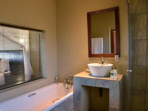 A bathroom with a bathtub, a sink, a mirror, and a shower area. - Mjejane River Lodge (Nkomazi)
