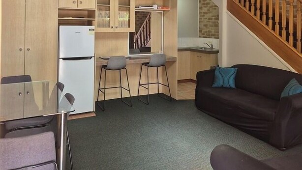 A compact apartment with a kitchenette, a dining area, a living room with a sofa, and a staircase leading to an upper level. - Country Gardens Motor Inn Toowoomba (South Toowoomba)
