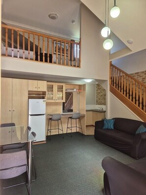 A compact apartment with a kitchenette, a dining area, a living room with a sofa, and a staircase leading to an upper level. - Country Gardens Motor Inn Toowoomba (South Toowoomba)