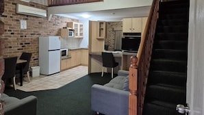 A compact living space with a kitchenette, a dining area, and a staircase leading to an upper level. - Country Gardens Motor Inn Toowoomba (South Toowoomba)