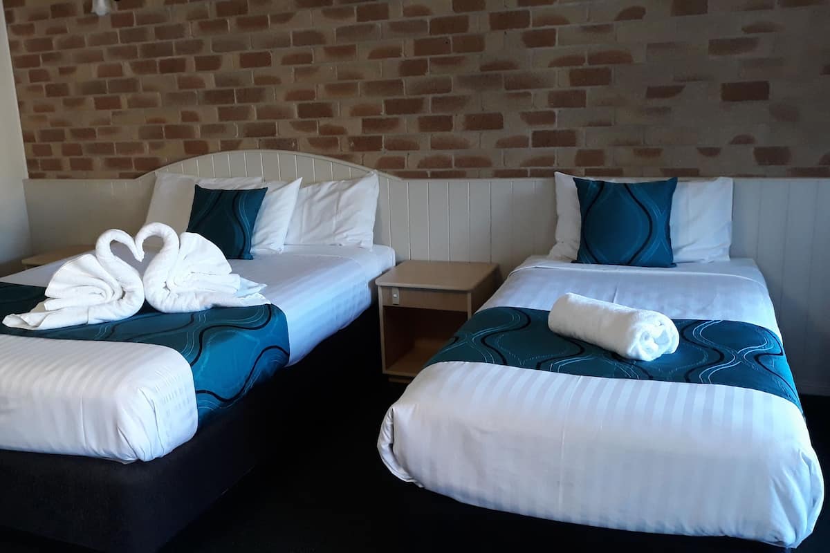 Two single beds with white linens and blue accents, a brick wall, and a wooden nightstand between them.