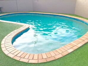 En swimmingpool med en kant av tegelstenar och konstgräs runt omkring.