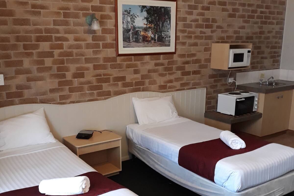 A hotel room with two beds, a small desk, a microwave, and a sink.