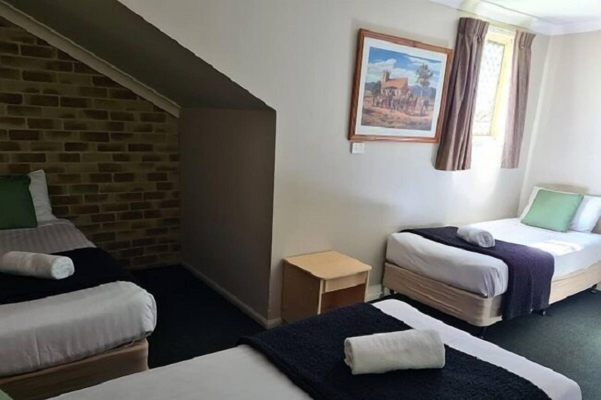 A hotel room with two single beds, a small wooden nightstand, a brick wall, and a painting on the wall.