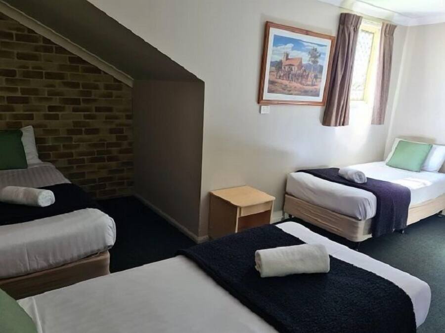A hotel room with two single beds, a small wooden nightstand, a brick wall, and a painting on the wall.