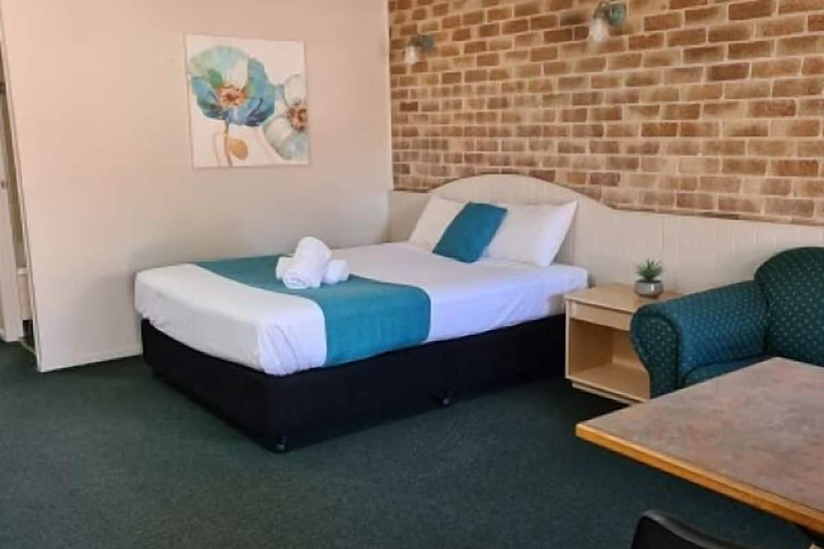 A single bed with a blue and white duvet, a small bedside table with a lamp, and a green armchair.