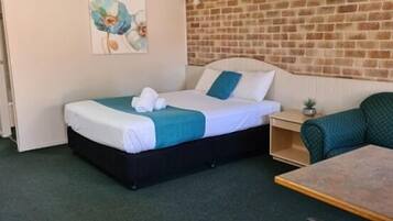 A single bed with a blue and white duvet, a small bedside table with a lamp, and a green armchair.