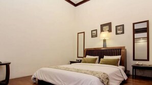 A hotel room with a large bed, wooden flooring, a nightstand with a lamp, and framed pictures on the wall. - Roemahkoe Heritage Hotel (Surakarta)