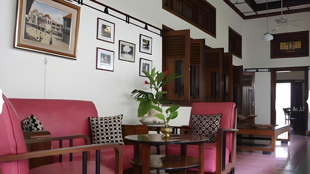 A modern living room with a pink sofa set, a round glass coffee table, and a potted plant. - Roemahkoe Heritage Hotel (Surakarta)