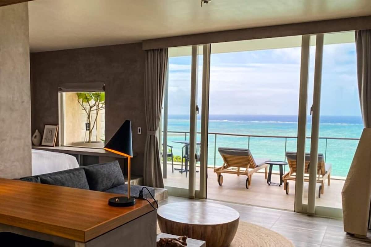 Een moderne hotelkamer met balkon, een ronde houten tafel, een bank en een televisie.