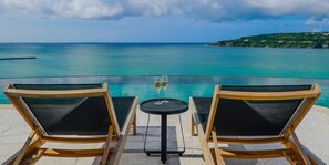 Two wooden lounge chairs and a small table with a glass of wine, overlooking a turquoise sea and a distant green hill. - KAYATSUMA OKINAWA HOTEL & RESORT (Nakijin)