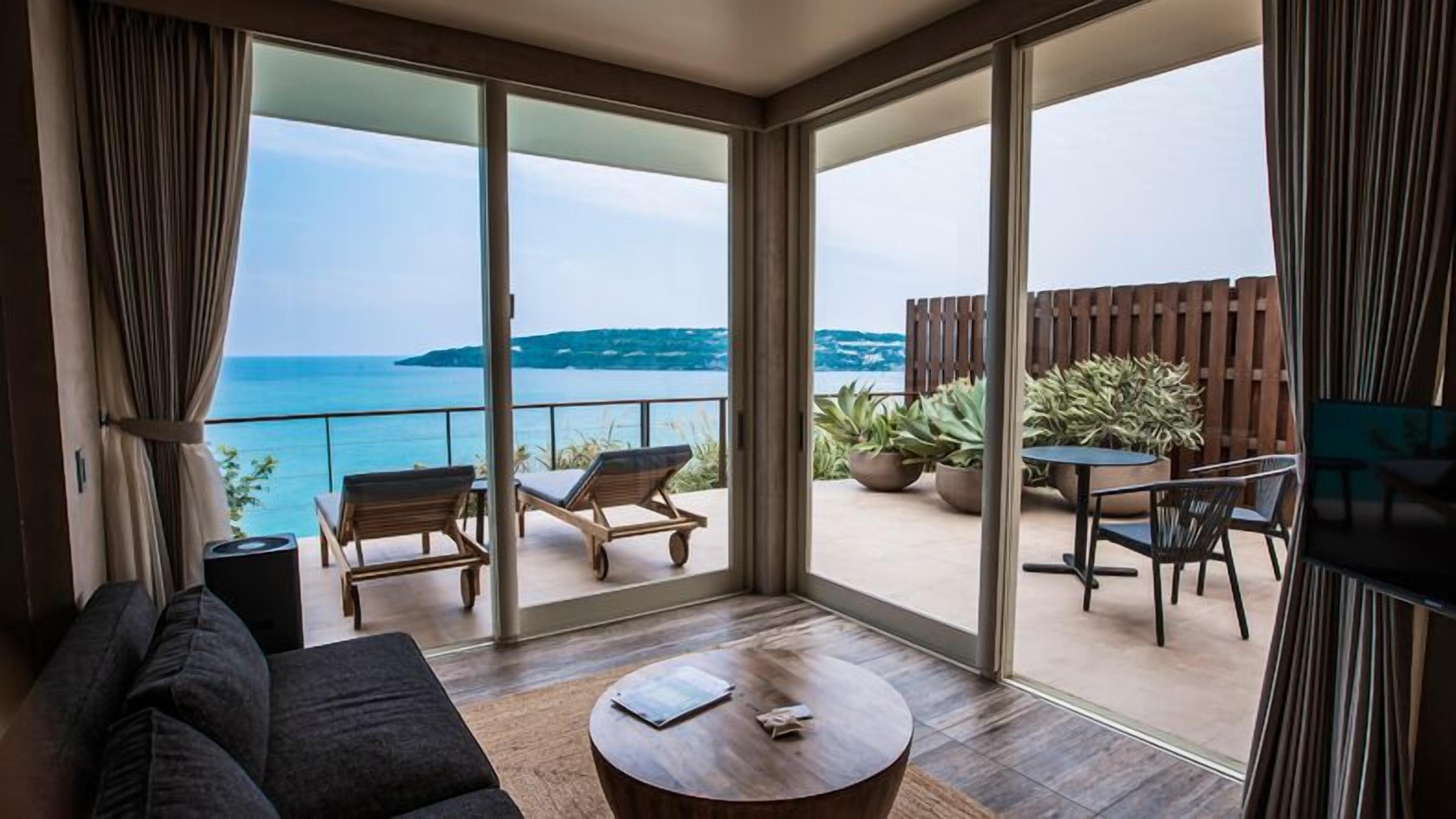 Een balkon met uitzicht op zee, een bank, een salontafel en een eethoek met stoelen en planten.