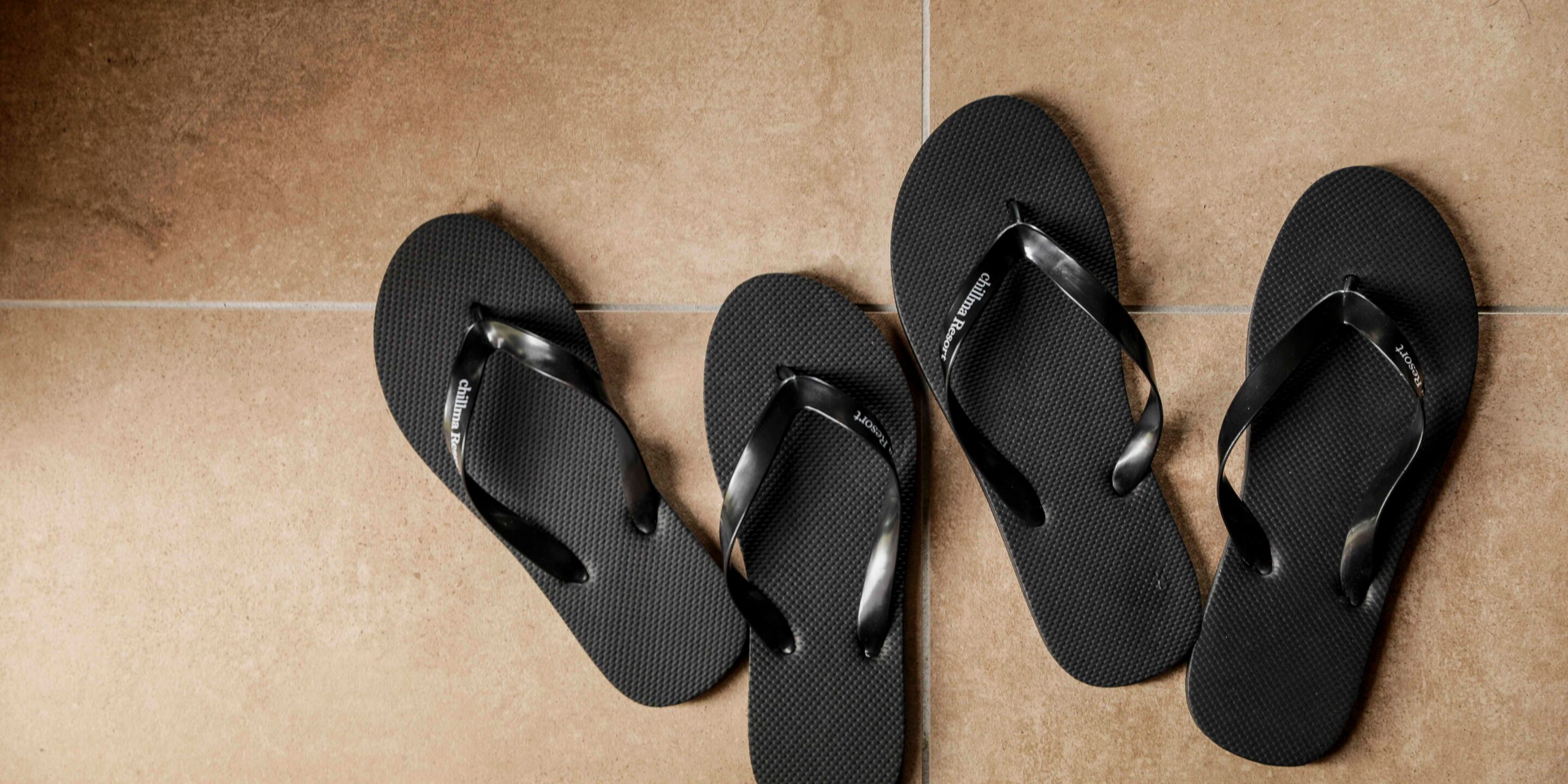 Drie paar zwarte slippers op een betegelde vloer.