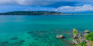 A coastal landscape with clear turquoise waters, rocky outcrops, and a distant hill with buildings. - KAYATSUMA OKINAWA HOTEL & RESORT (Nakijin)