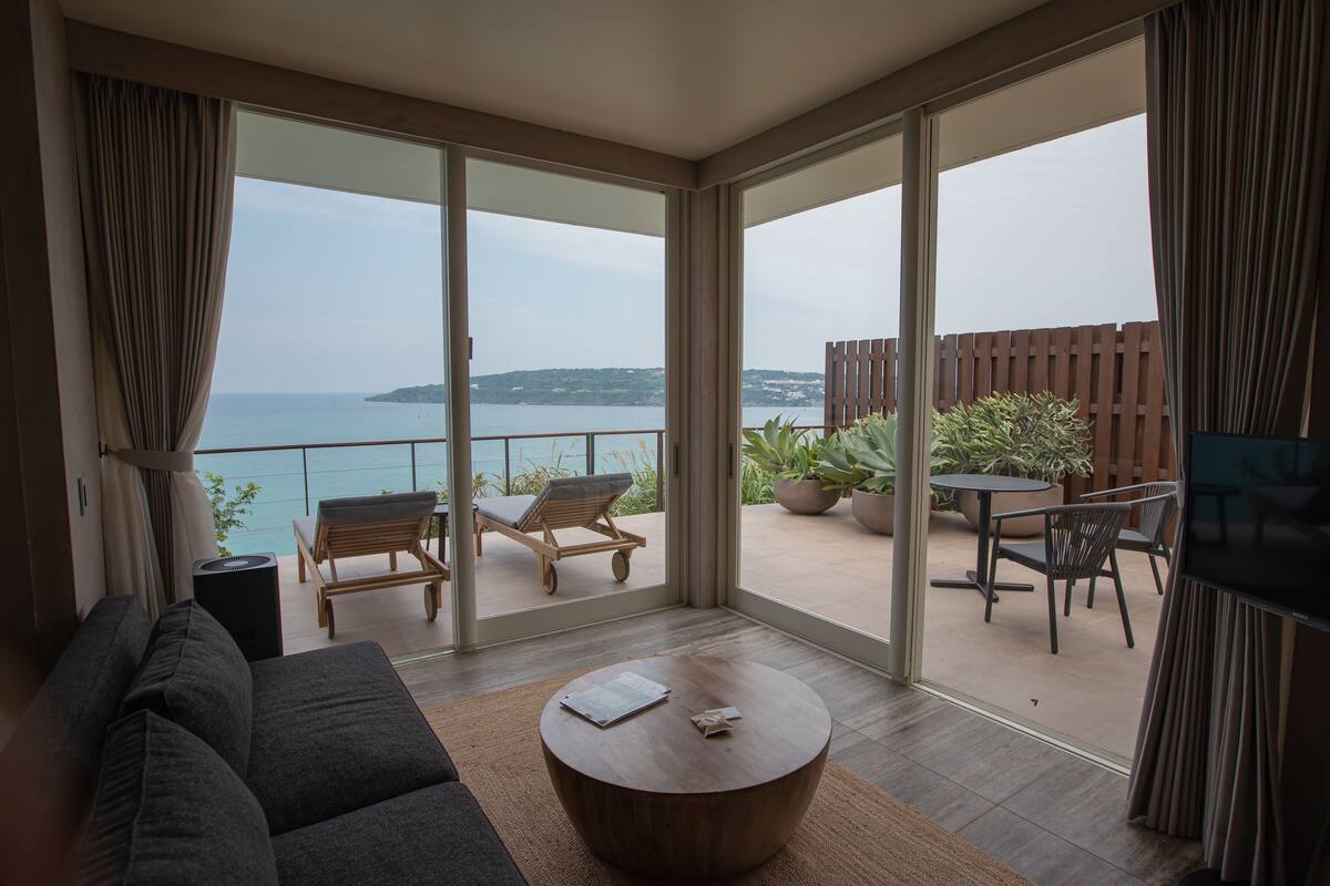 Een moderne woonkamer met een bank, een salontafel en een balkon met tuinmeubilair en uitzicht op zee.