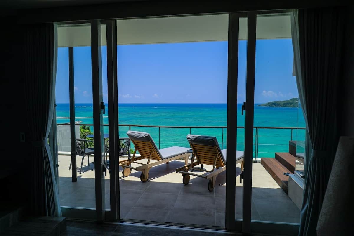 Een balkon met twee loungesteunen en een tafel, met uitzicht op een turquoise oceaan en een heldere lucht.