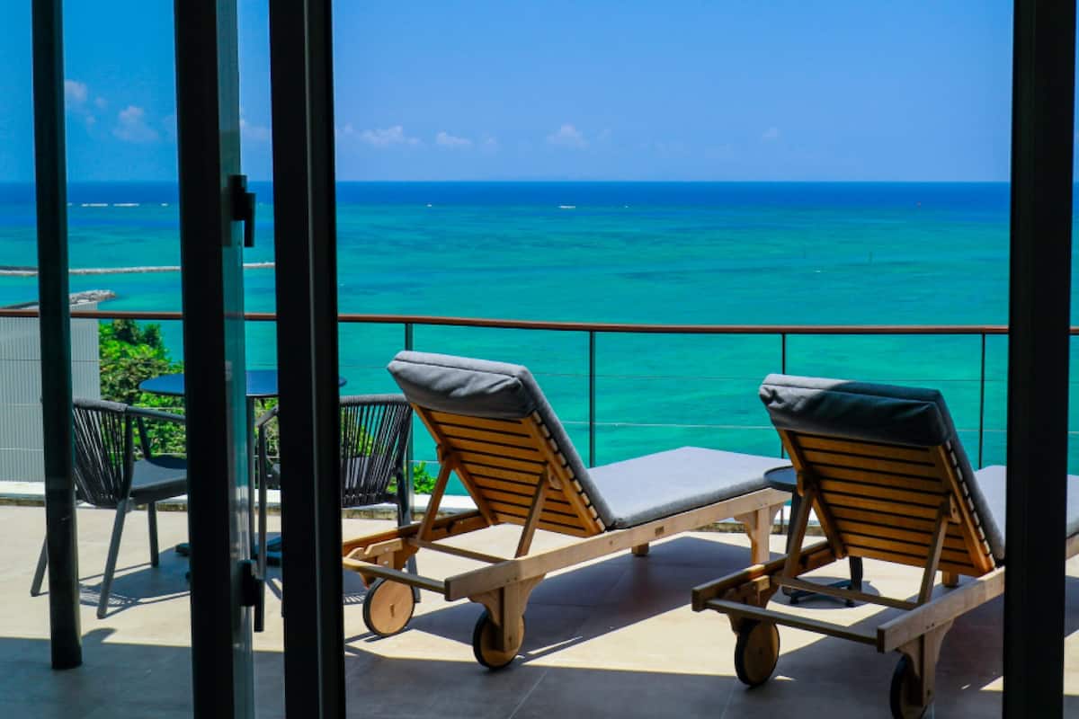 Een balkon met twee loungestoelen, gericht op uitzicht op een turquoise oceaan.