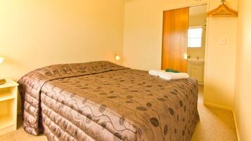 Un dormitorio con una cama grande, una mesita de noche, un perchero y un baño visible a través de una puerta abierta.