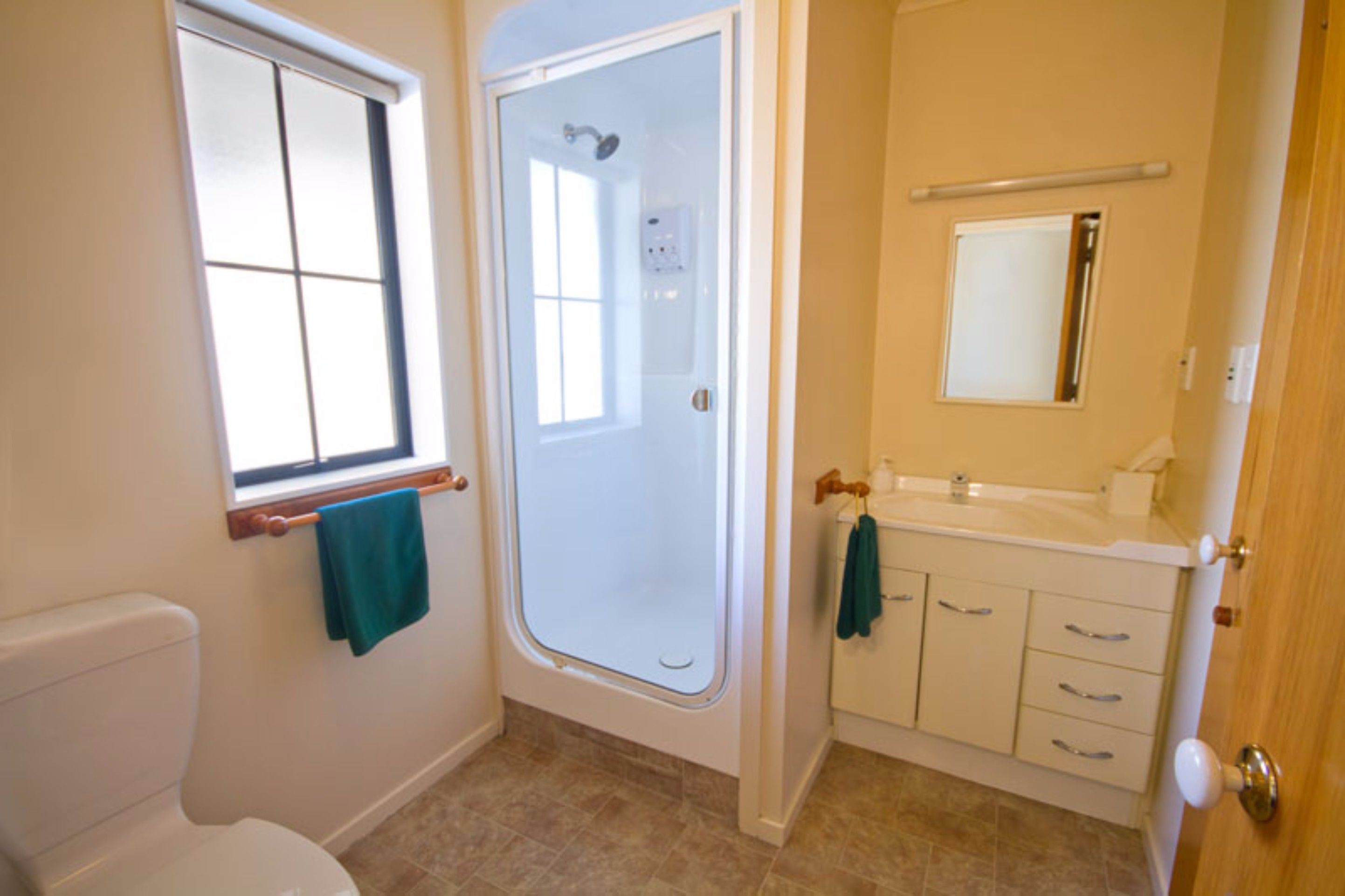 A bathroom with a toilet, a shower enclosure, a sink with a mirror, and a window.