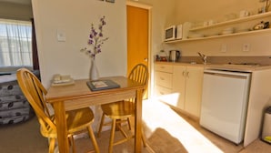 Een compacte keuken met een magnetron, fornuis en koelkast. Er is een eettafel met stoelen en een vaas met bloemen.