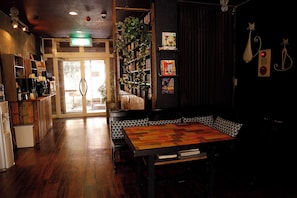 A cozy cafe with a wooden table and benches, a coffee machine, and a bookshelf with various items. - Pension Papermoon (Nasu)