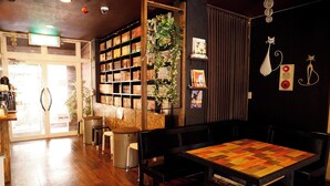 A cozy cafe with wooden flooring, a central table with chairs, a bookshelf, and decorative wall art.