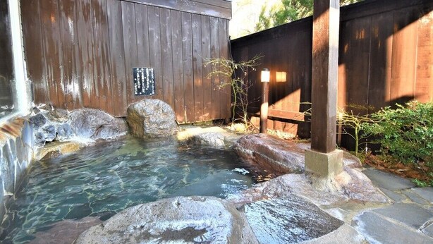 A hot spring area with stone steps leading into the water, surrounded by wooden fences and a wooden structure.