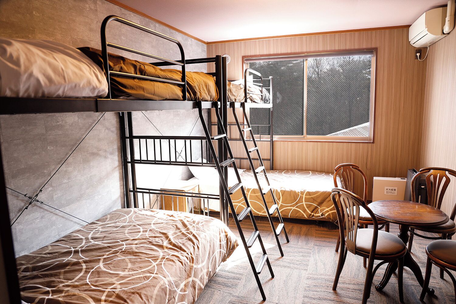 A dormitory room with bunk beds, a desk, chairs, and a window.