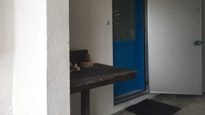 A door with a blue frame, a small table with a statue, and a doormat. - Life Rock (Chatan)