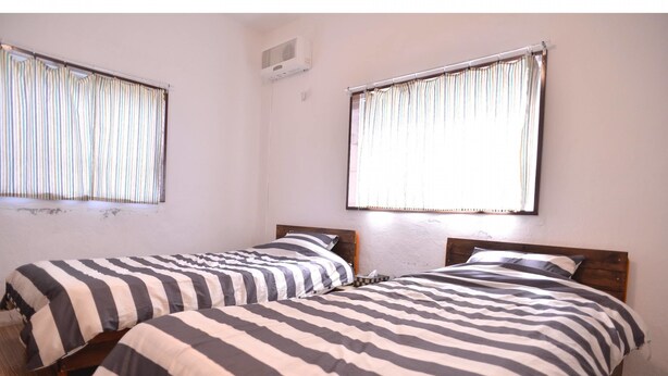 A room with two beds, each with striped bedding, a window with blinds, and a ceiling fan. - Life Rock (Chatan)