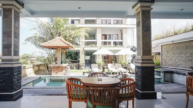 A poolside area with a wooden table and chairs, a small gazebo, and a view of a multi-story building. - Agung Homestay Canggu (Canggu)