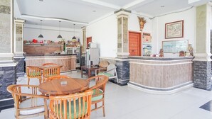 A spacious dining area with a wooden table and chairs, a kitchen area with a counter and appliances, and a reception desk with a stone column. - Agung Homestay Canggu (Canggu)