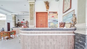 A reception area with a wooden door, a reception desk, and a dining area with a table and chairs. - Agung Homestay Canggu (Canggu)