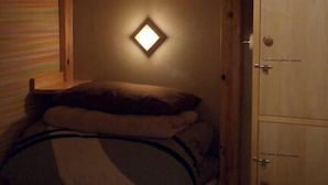 Ein Etagenbett mit kleinem Fenster, Holzwänden und einem Kleiderschrank.