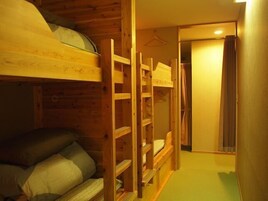 Una habitación con literas, paredes de madera y un pasillo que lleva a una puerta.