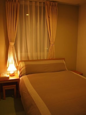 A hotel room with a bed, a nightstand, a lamp, and curtains.
