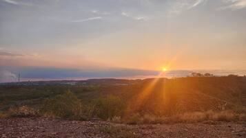 Auringonlasku kumpuilevan maiseman yllä, etualalla näkyy soratie.