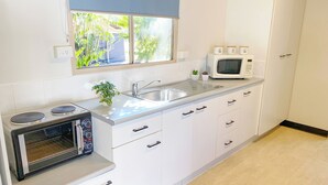 Una cocina moderna con armarios blancos, horno empotrado, microondas y ventana con vista a la vegetación.