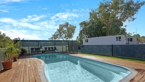 Una piscina rectangular con cubierta de madera, rodeada por una valla y árboles.