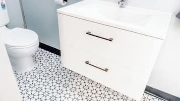A bathroom with a white sink, two drawers, a toilet, and a patterned floor.