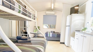 Una habitación de hotel compacta con literas, una kitchenette pequeña, una mesa de comedor y una planta en maceta.