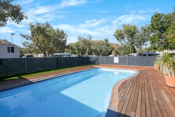 A rectangular swimming pool with a wooden deck surrounding it, enclosed by a metal fence.