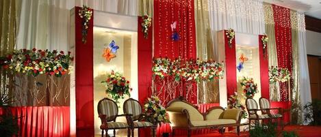 Un escenario con cortinas rojas, arreglos florales y asientos.