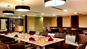 A dining area with a long table set for a meal, surrounded by chairs, and overhead lighting fixtures. - Orchardz Ayani (Pontianak)