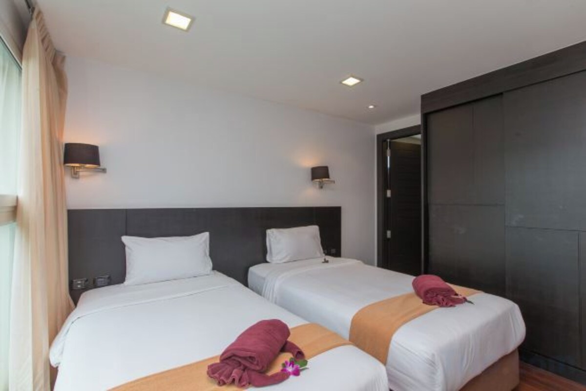 A hotel room with two beds, a dark headboard, and a door to a dark room.
