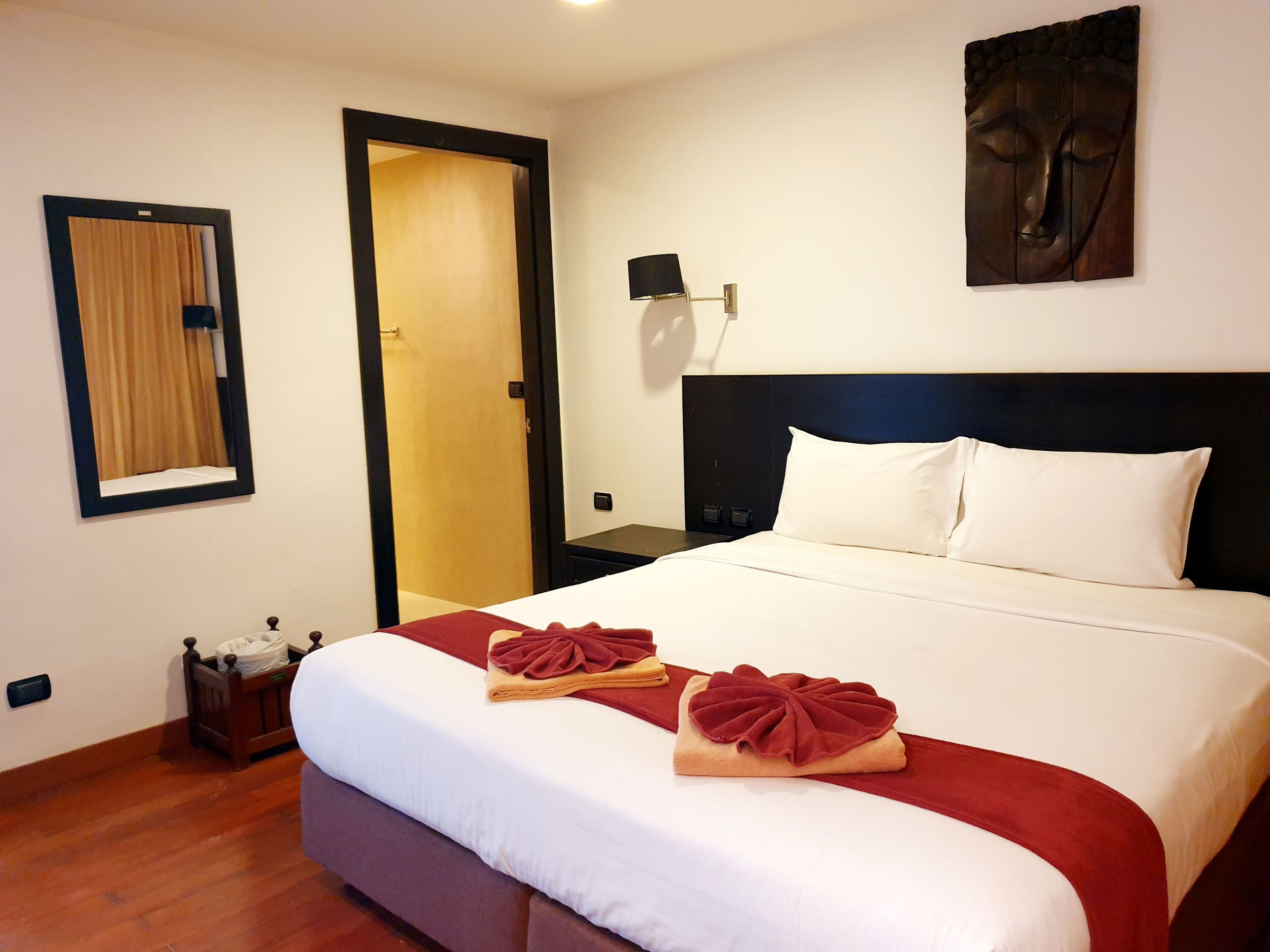 Habitación de hotel con una cama grande, una mesita de noche de madera, un espejo y una obra de arte colgada en la pared.