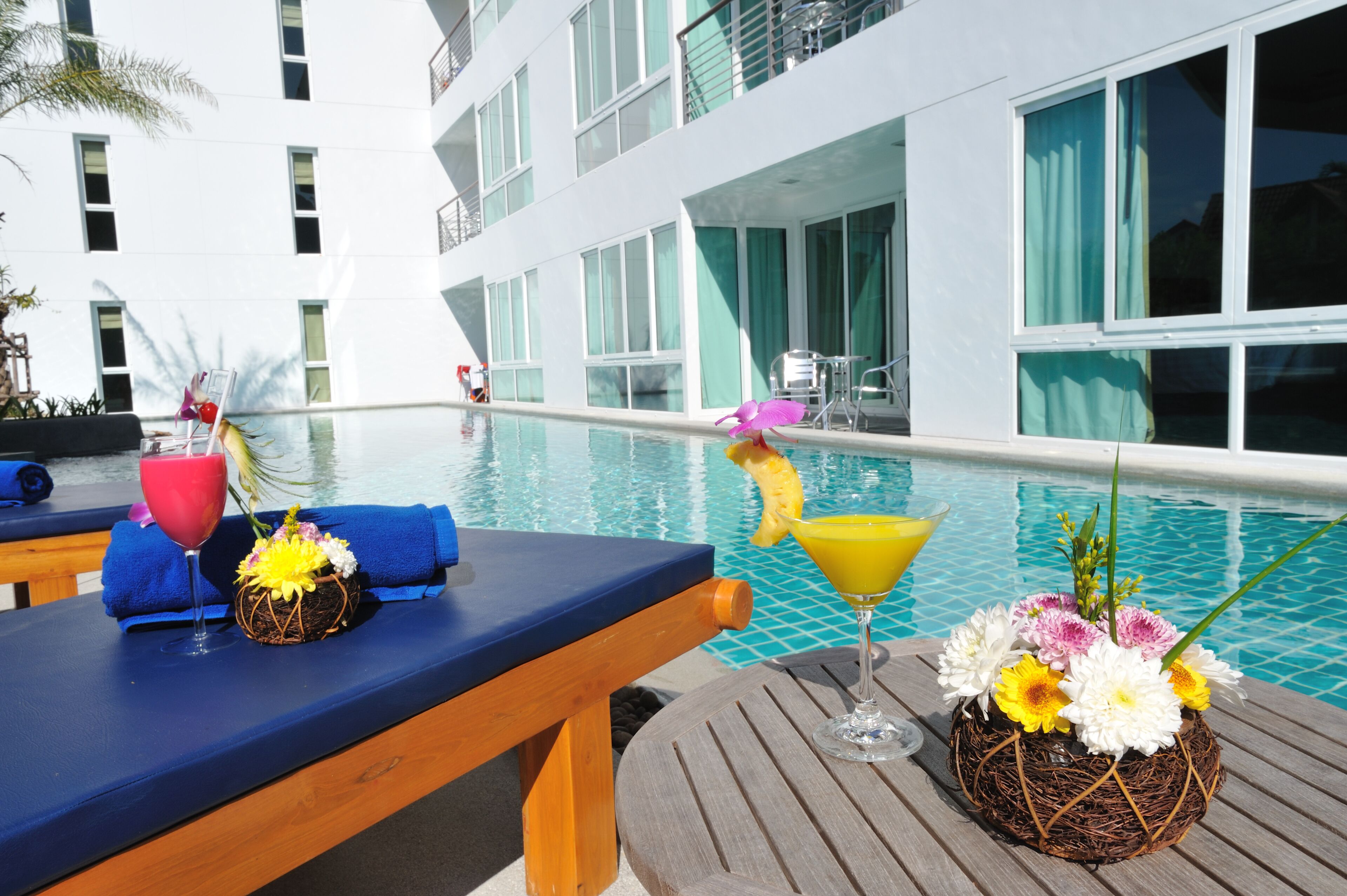 A poolside area with lounge chairs, a pool, and a building with large windows in the background.