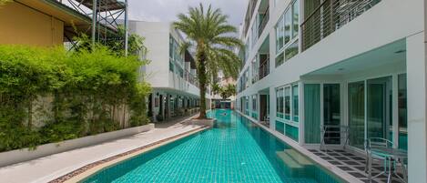 A swimming pool with a tiled floor, surrounded by buildings with balconies and windows.
