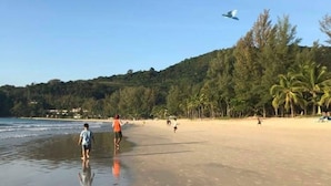 A beach with footprints in the sand, palm trees, and a clear sky. - The Palms Kamala Beach (Kamala)